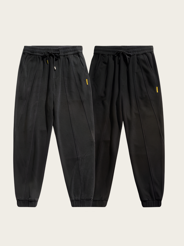 Two pairs of black jogger pants on a light beige background