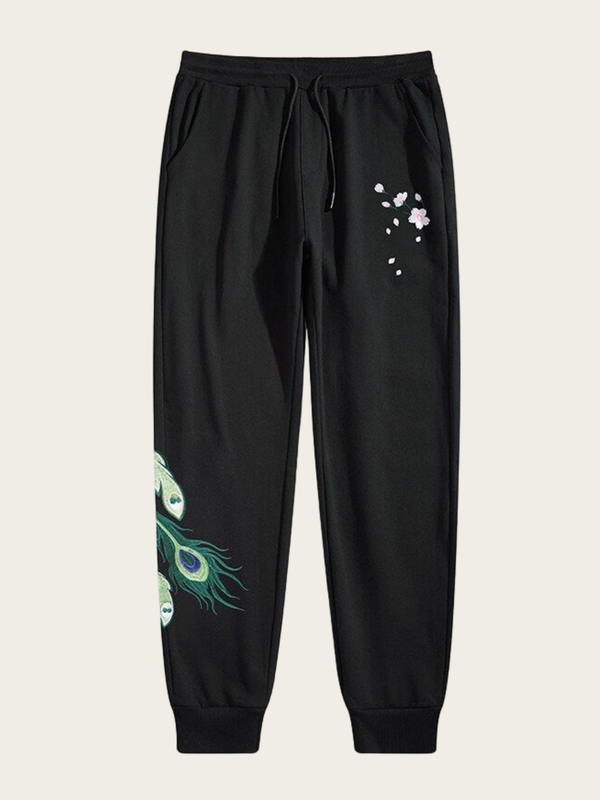 Black sweatpants with peacock feather design on a beige background