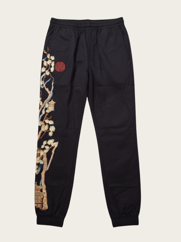 Black jogger pants with floral embroidery on a beige background