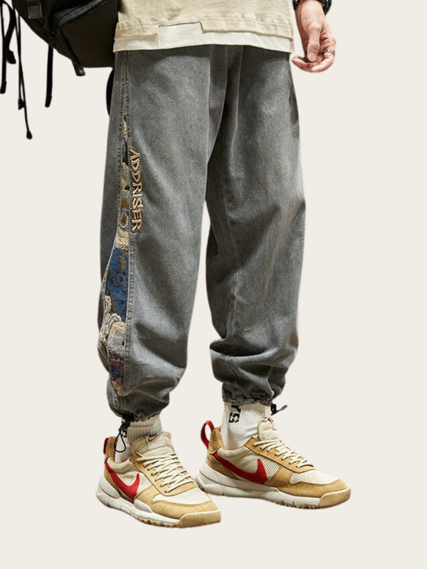 Person wearing gray jogger pants with a brand logo and beige sneakers with red accents on a light background
