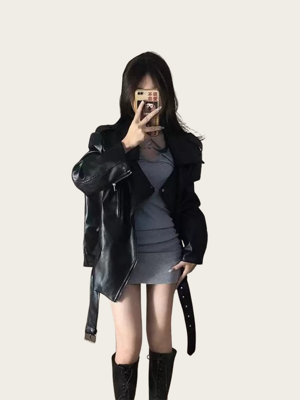 Person wearing a black leather jacket, gray top, and skirt with knee-high boots on a plain background