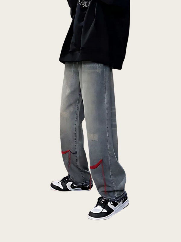 Person wearing gray jeans with red accents and black sneakers on a white background