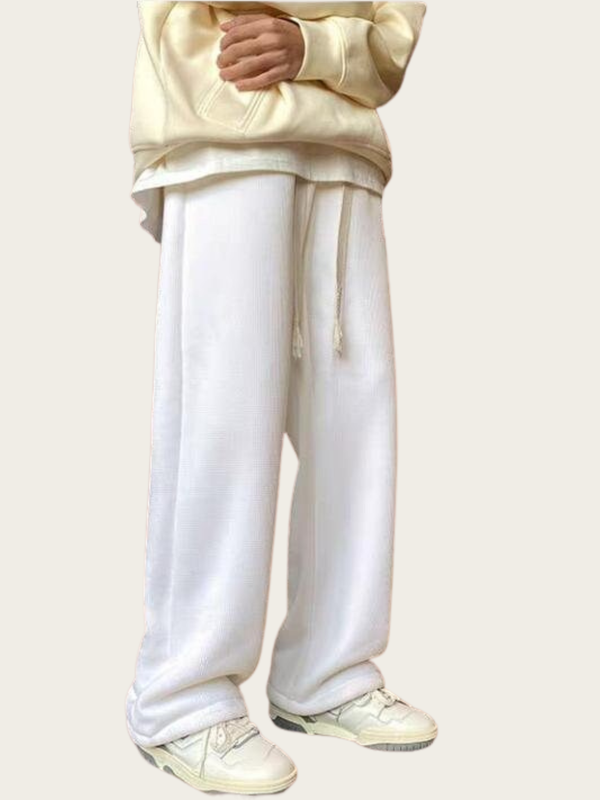 Person wearing a beige hoodie and white pants on a plain background