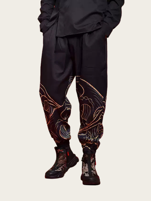 Person wearing black pants with intricate floral patterns and black boots on a beige background