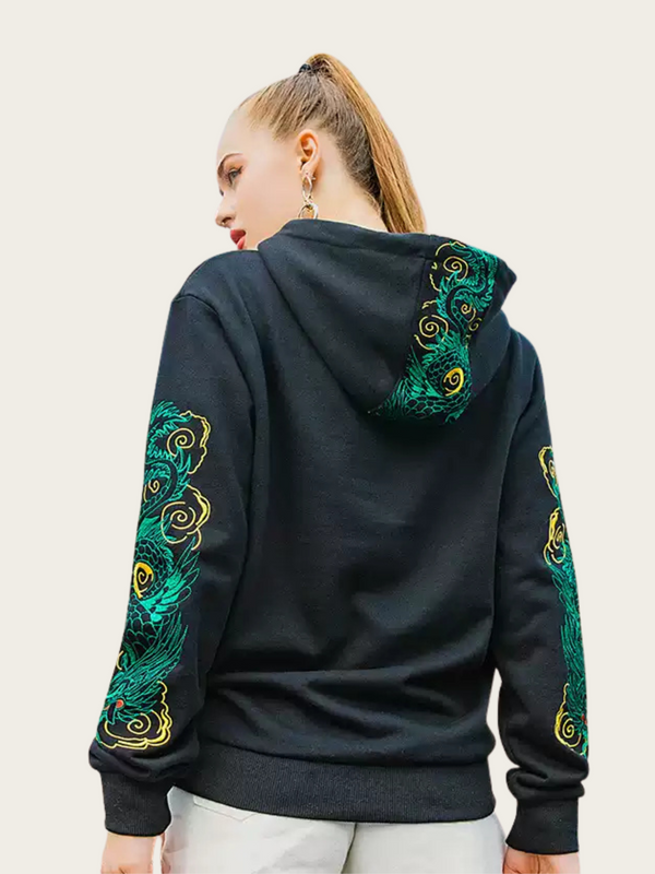 Person wearing a black hoodie with green and gold embroidery on sleeves and back against a light background