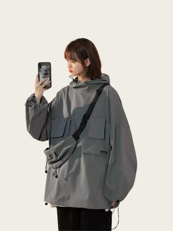 Person wearing a gray jacket with a black strap taking a selfie on a light gray background