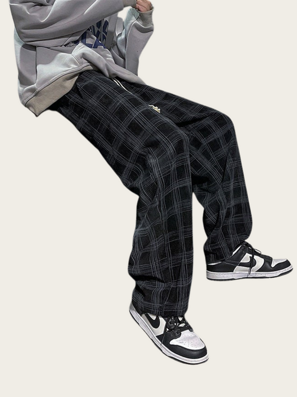 Person wearing black plaid pants and black and white sneakers on a white background