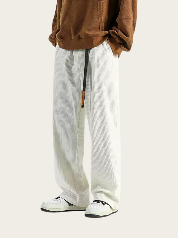 Person wearing a brown jacket, white pants, and black shoes on a light background