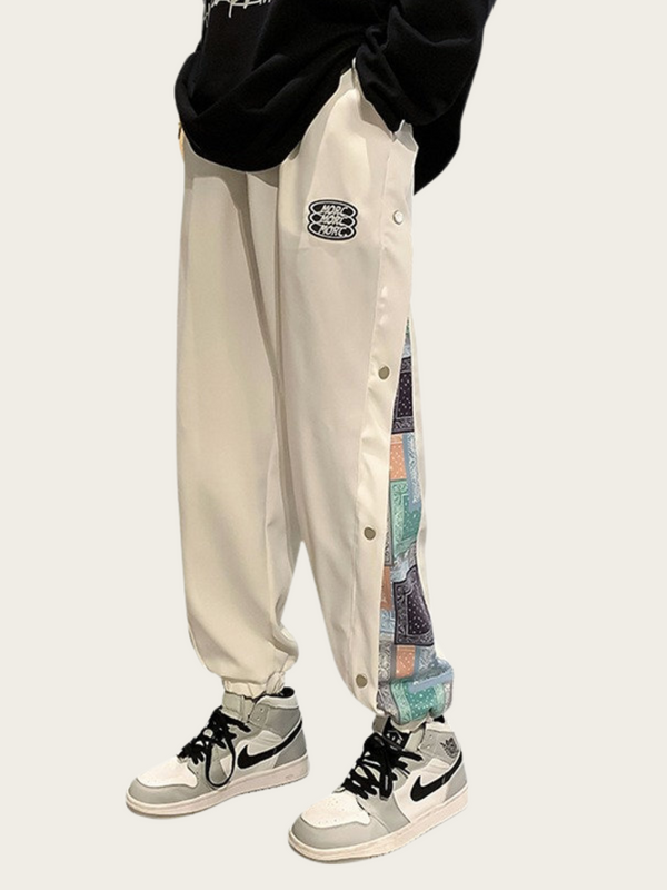 Person wearing beige pants with colorful patchwork design and black sneakers on a white background