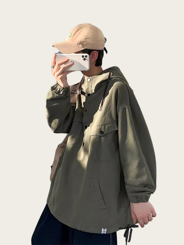 Person wearing a green jacket and beige cap holding a phone on a plain background