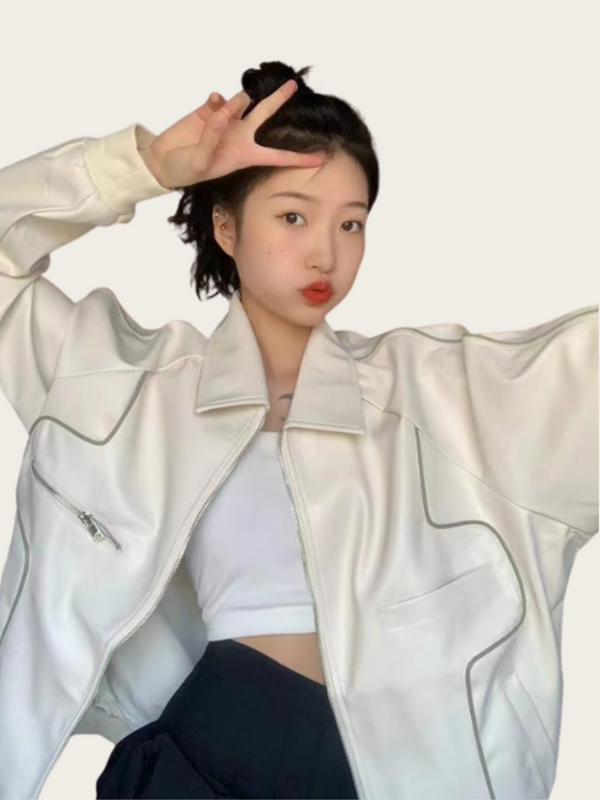 Person wearing a light-colored jacket over a white top and dark pants on a plain background