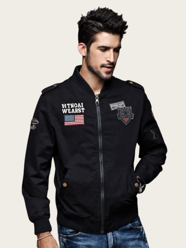 Man wearing a black jacket with patches on a light gray background