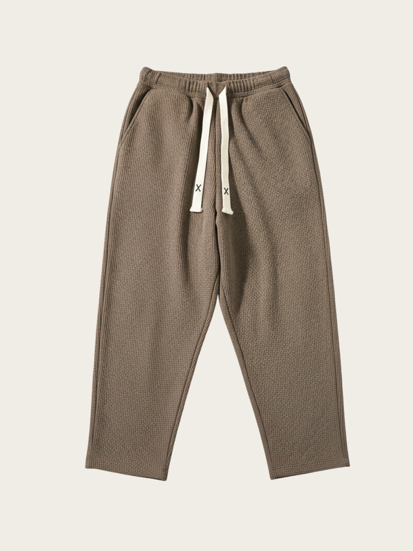 Brown sweatpants with white drawstrings on a beige background