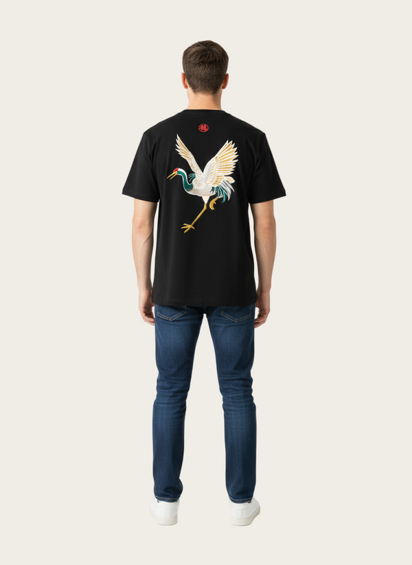 Person wearing a black t-shirt with a colorful bird design on the back, standing against a white background.