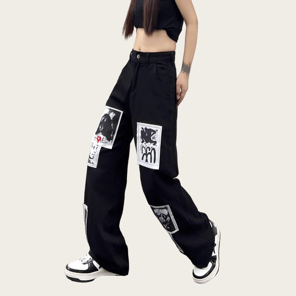 Person wearing black pants with graphic designs against a yellow wall.