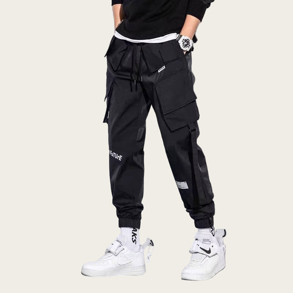 Person wearing black cargo pants with white text and white sneakers on a yellow background