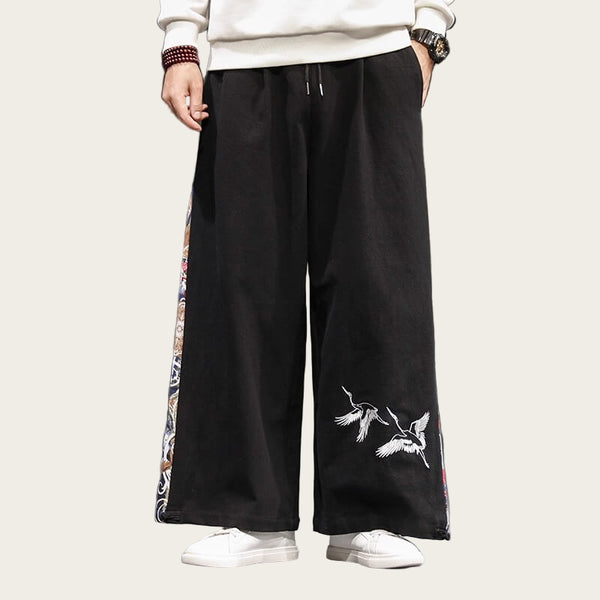 Person wearing black wide-leg pants with bird embroidery