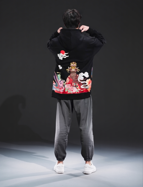 Person wearing a black hoodie with colorful floral designs and gray pants on a dark background