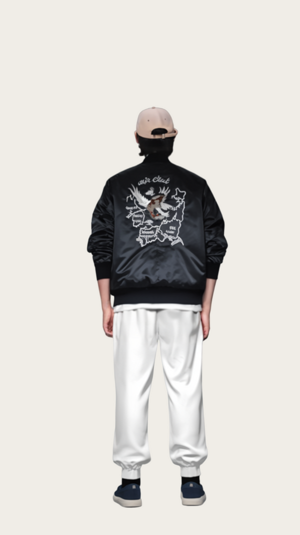 Person wearing a black jacket with white designs on the back, standing against a gray background