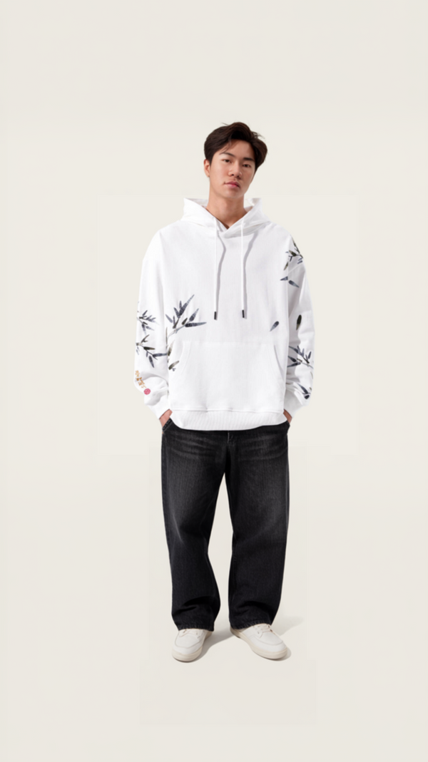 Person wearing a white hoodie with black patterns and dark pants on a plain background