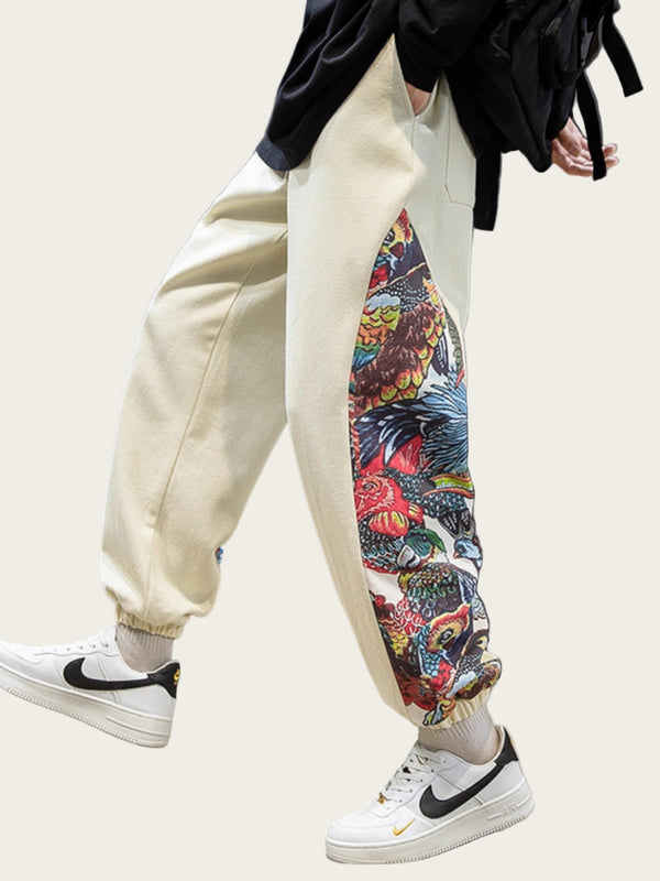 Person wearing beige jogger pants with a colorful bird design, white sneakers, and a black jacket.