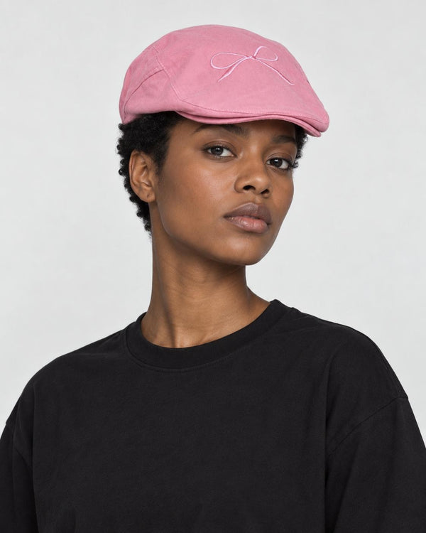 Model wearing the pink bow embroidered flat cap with a black tee, three-quarter view