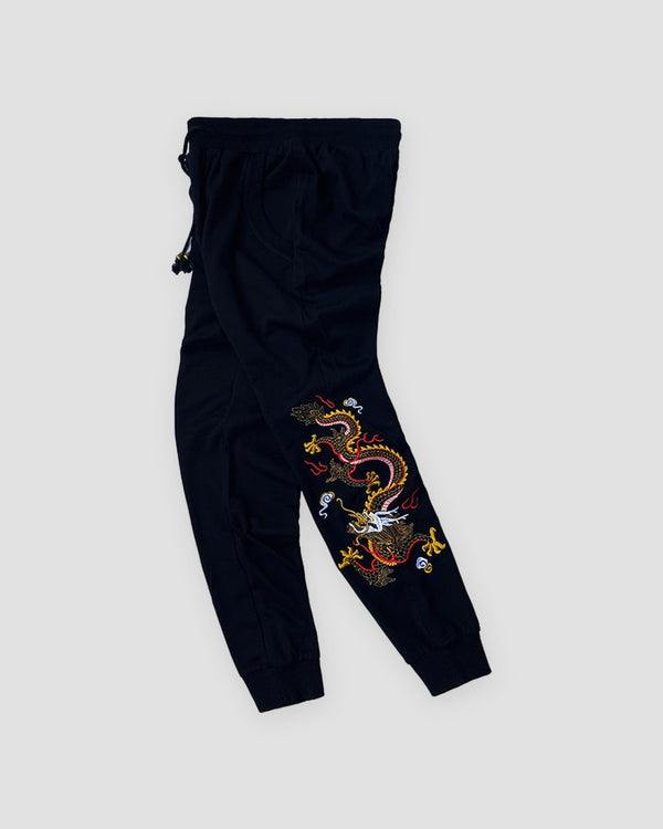 Black jogger pants with a dragon embroidered down one lower leg, front view