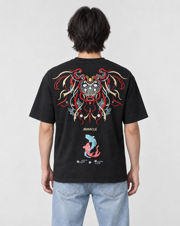 Man seen from behind in the black T-shirt with a large embroidered lion-dog mask, the word MIRACLE and two koi on the back