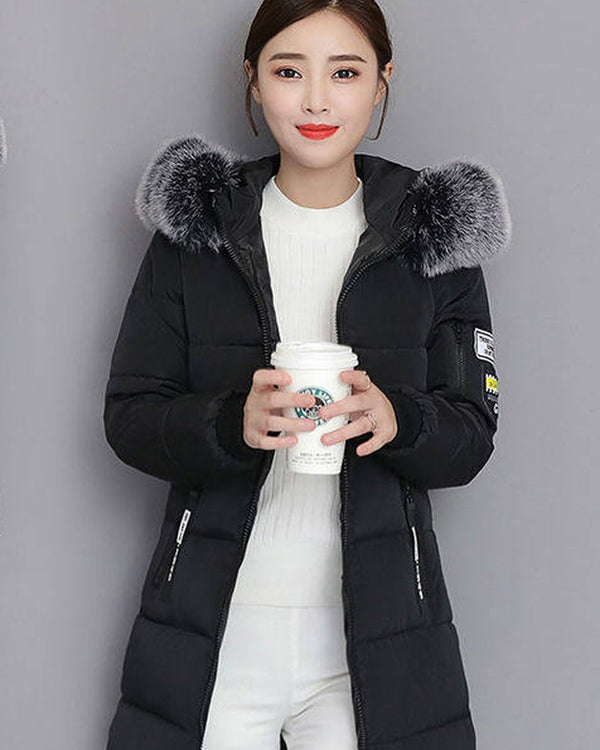 Black long puffer coat with a dark gray faux-fur collar, worn with white pants, shown from the front and three-quarter
