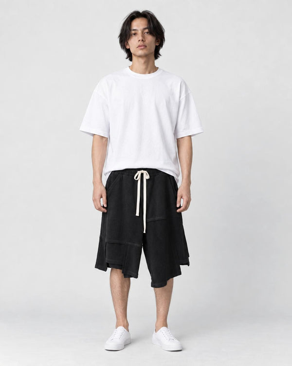 Man in black asymmetric knee-length shorts with an uneven hem, white tee and white sneakers