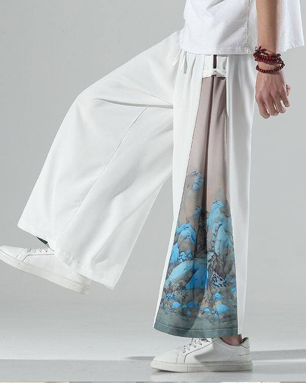 Ivory white wide-leg pants in motion, with a pink-beige side panel and a blue mountain landscape at the hem