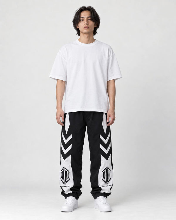 Man in black joggers with white chevron panels on the thighs and white lower legs, white tee and sneakers, full length