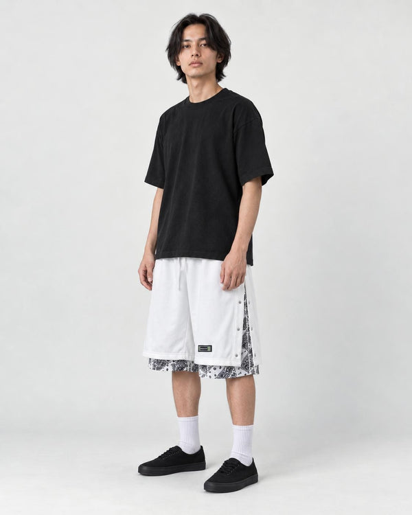 Model wearing the white layered paisley snap-side shorts with a black tee and black sneakers, three-quarter view