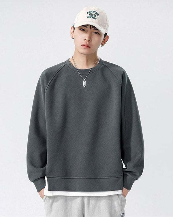 Dark gray raglan sweatshirt with a white layer showing below the hem, worn with a white cap and gray pants