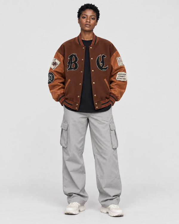Model wearing the brown playing card patch varsity jacket, front view with B and C letters