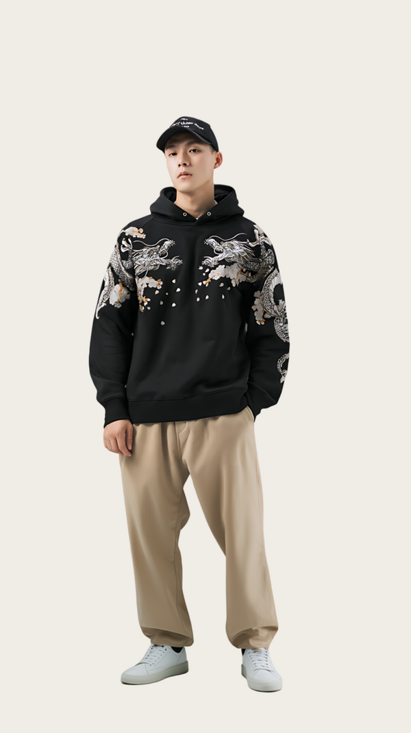 Person wearing a black hoodie with floral patterns and beige pants on a gray background
