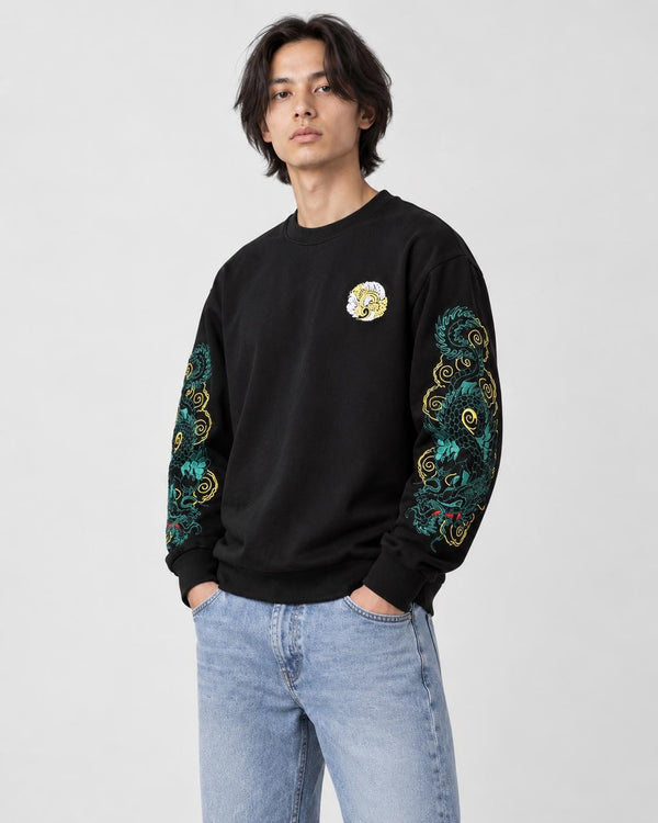 Model wearing the black twin dragon sleeve sweatshirt with light-wash jeans, three-quarter view
