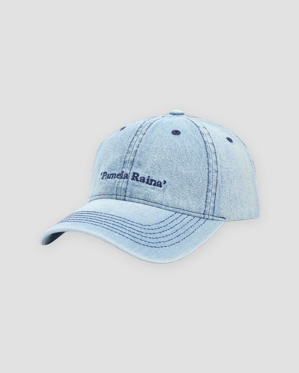 Light blue washed denim baseball cap with navy Pamela Raina lettering on the front