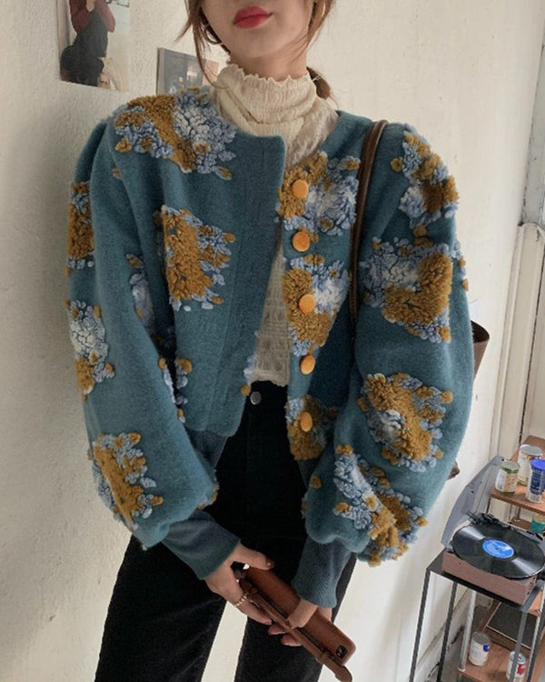 Woman in the teal cropped jacket with raised yellow and pale blue flower patches, gold buttons and a white lace collar
