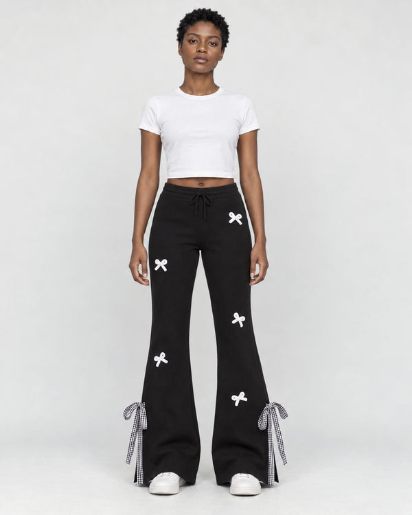 Woman in black flared sweatpants with small white bows, a white cropped tee and white sneakers, full length
