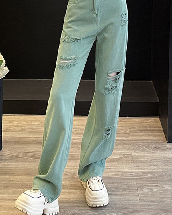 Faded mint-green wide-leg jeans with frayed rips on the thigh and knee, worn standing