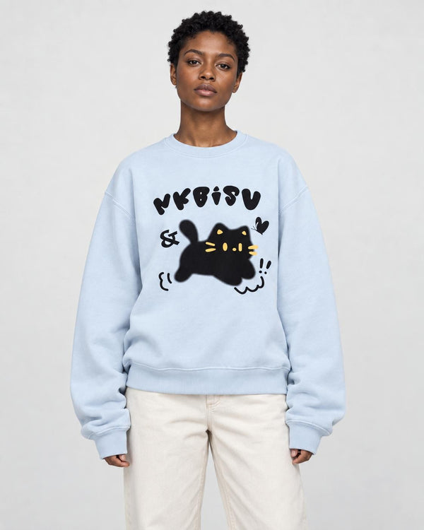 Woman in a light blue loose sweatshirt with a black cat print, cream trousers and white sneakers