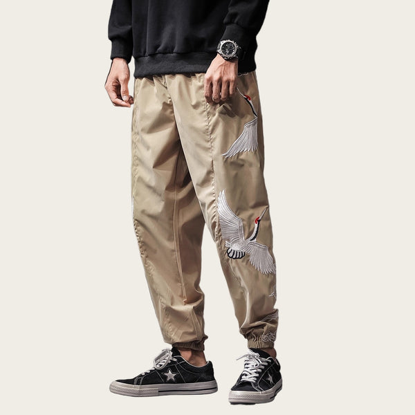 Person wearing beige pants with white bird embroidery, standing in a room.