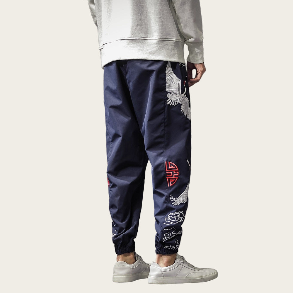Person wearing navy pants with white and red embroidery in a room setting.