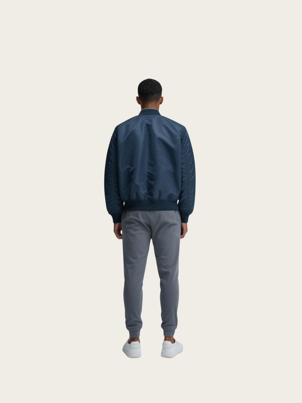 Person wearing a navy bomber jacket and gray pants on a white background