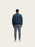 Person wearing a navy bomber jacket and gray pants on a white background
