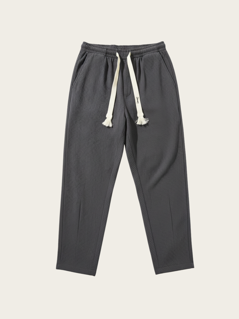 Dark gray jogger pants with white drawstring on a light beige background