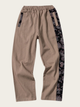 Beige pants with black floral side panels on a beige background