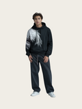 Person wearing a black and white hoodie with dark jeans on a light gray background