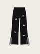 Black pants with white floral patterns and gray suspenders on a light beige background